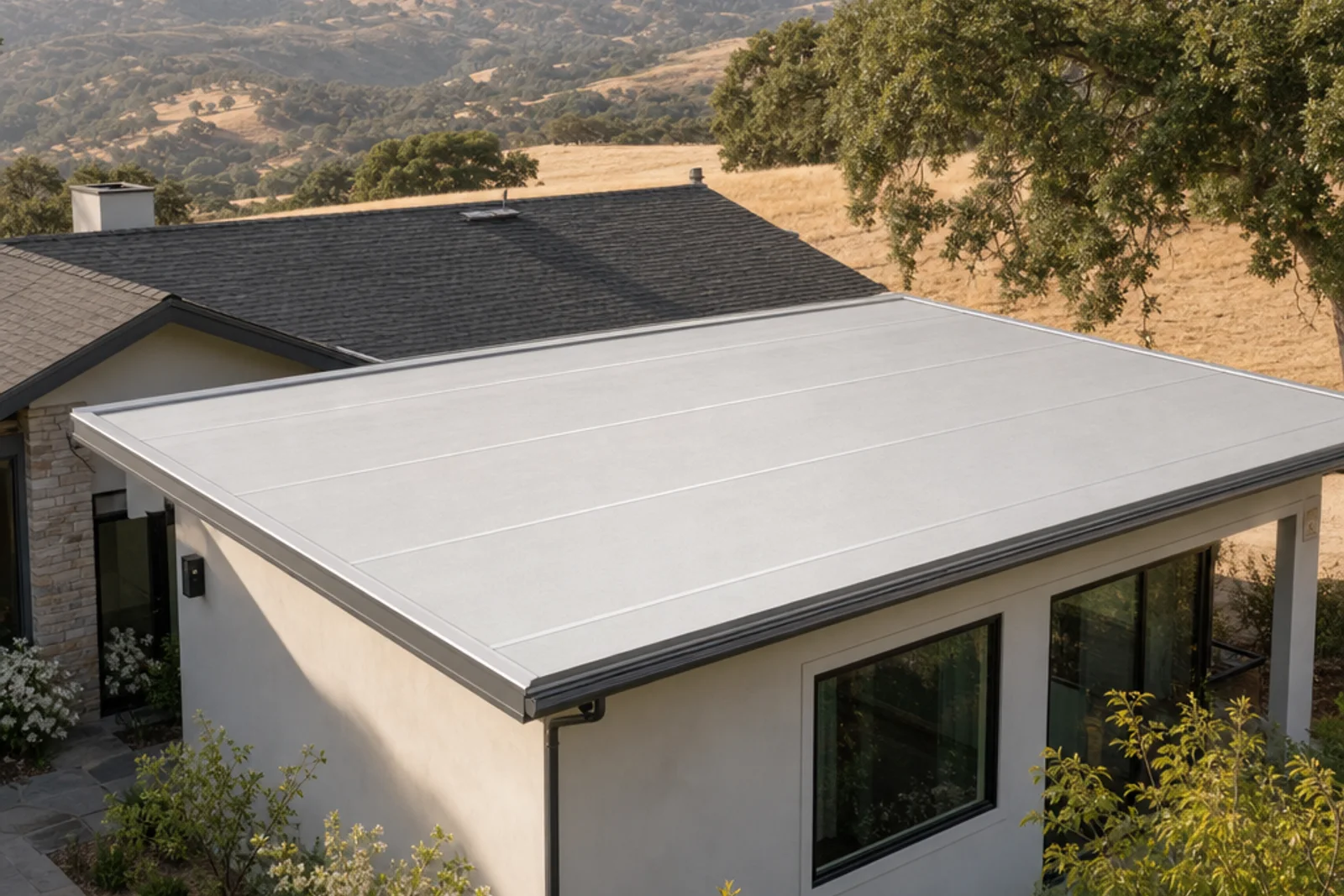Light-colored low-slope roof on a contemporary stucco home in an oak-covered foothill setting.