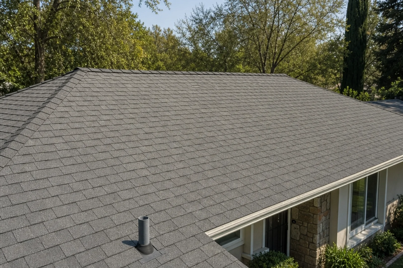 Composition-shingle ranch roof with pipe flashing and mature trees on a level lot.